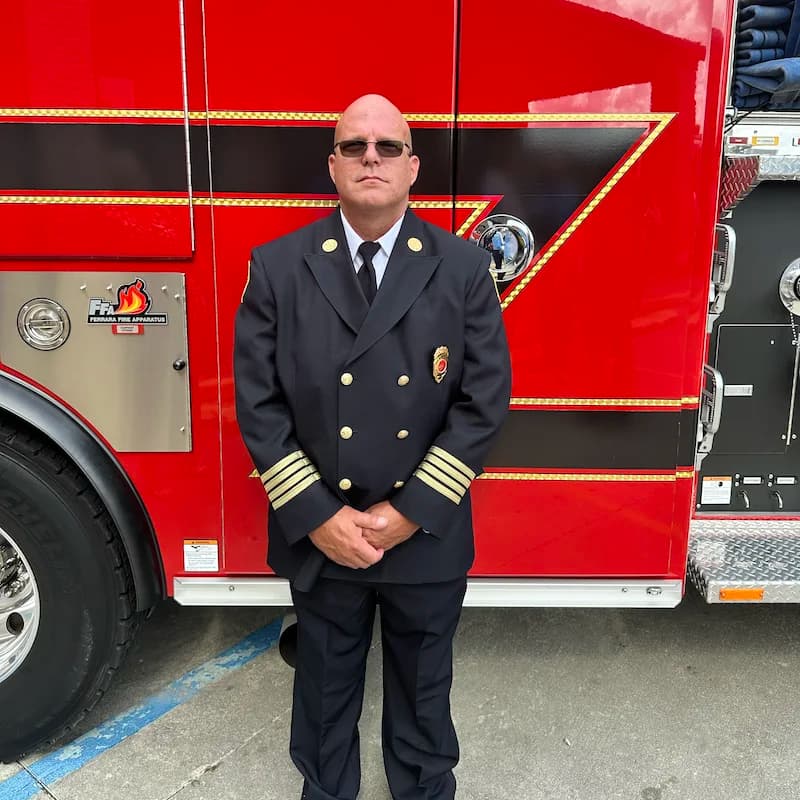 Clint L. Sanchez in his Baton Rouge Fire Department dress uniform, standing in front of a fire engine