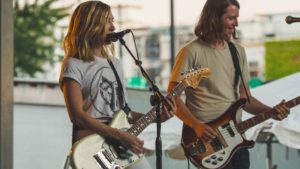 female guitarist and male bassist singing in a band onstage 1
