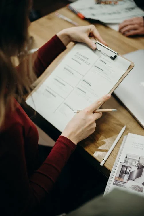 A coach sits at a desk reviewing documents on a clipboard, representing the actual process of evaluating athlete recruiting submissions.