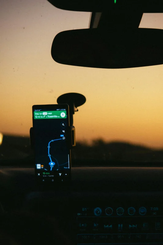 A smartphone mounted on a car dashboard displays a GPS navigation route map, representing how route optimization software is used by field service operators in a work vehicle.