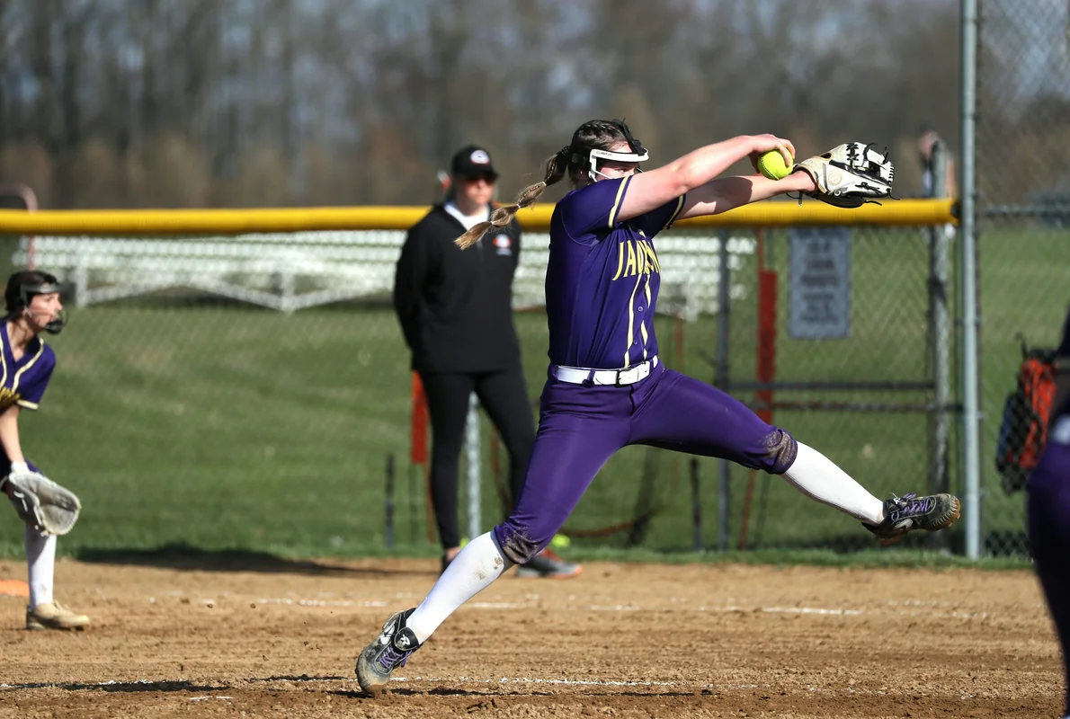 A softball player winds up for a throw on a bright green infield during a travel ball game.