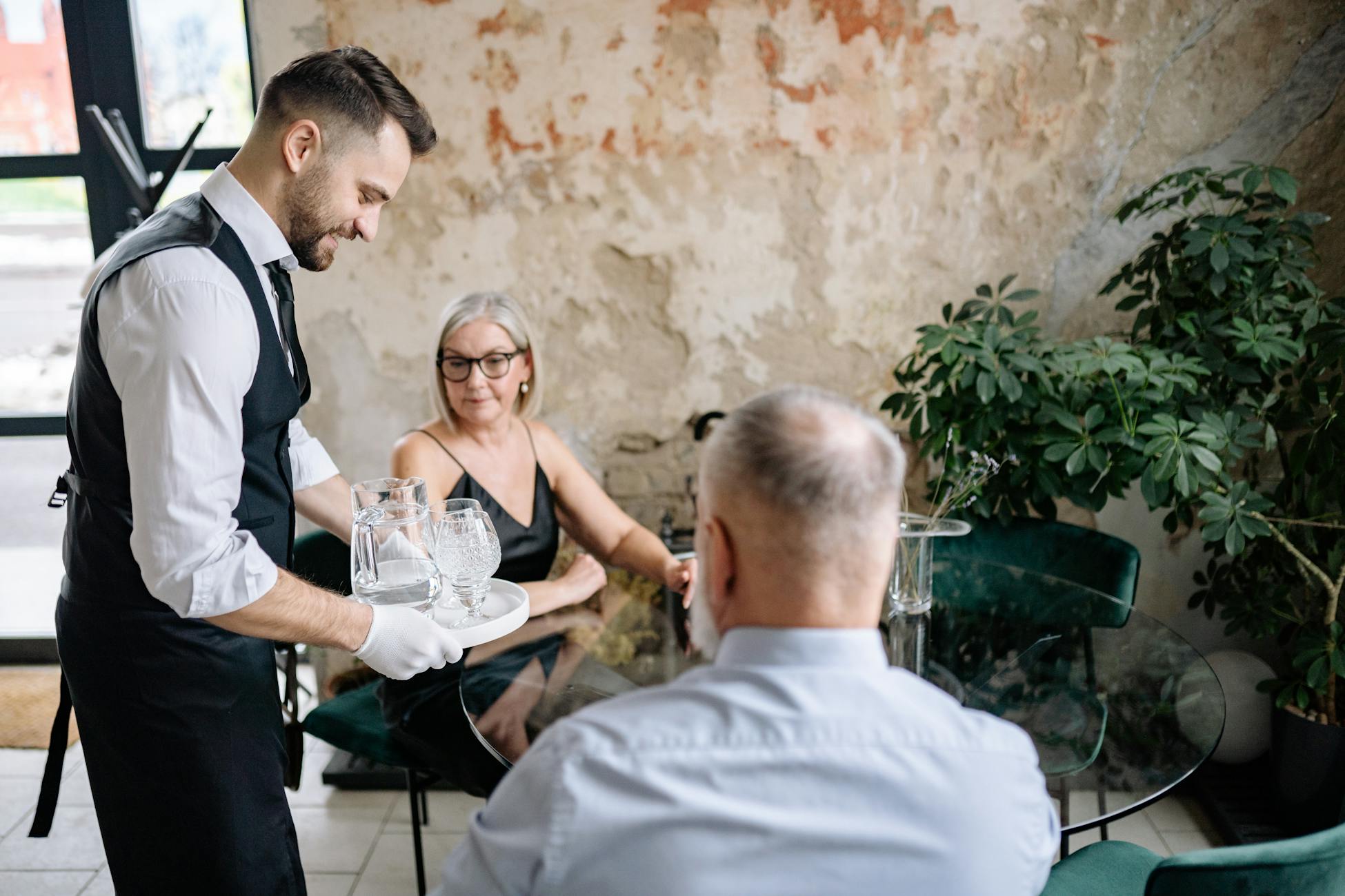 Waiter in a black apron interacting warmly with a senior couple at a restaurant table