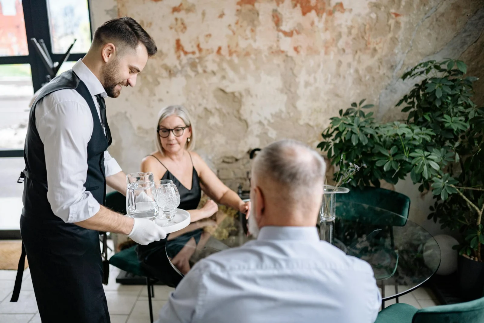 Waiter in a black apron interacting warmly with a senior couple at a restaurant table